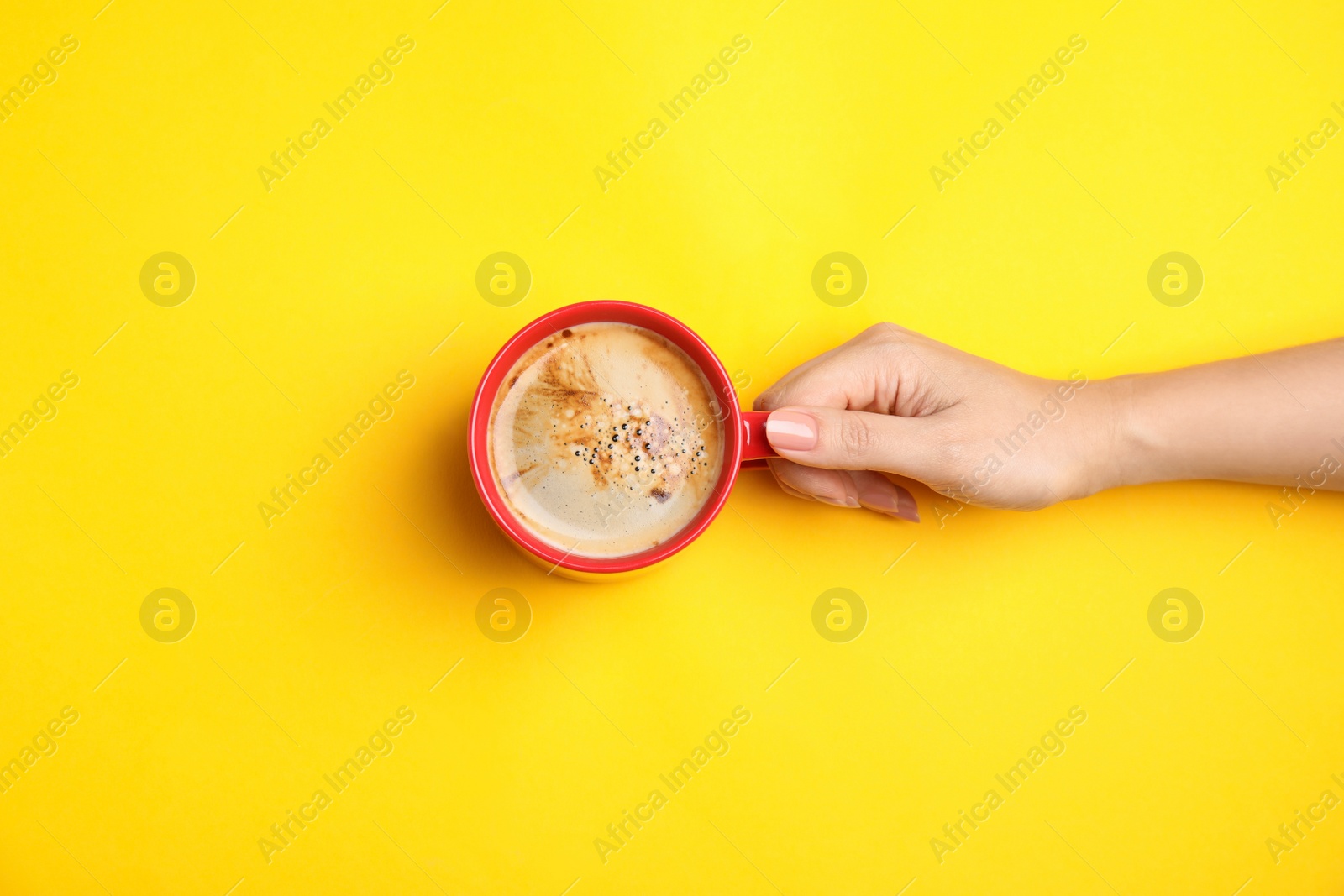 Photo of Woman with cup of coffee on yellow background, top view