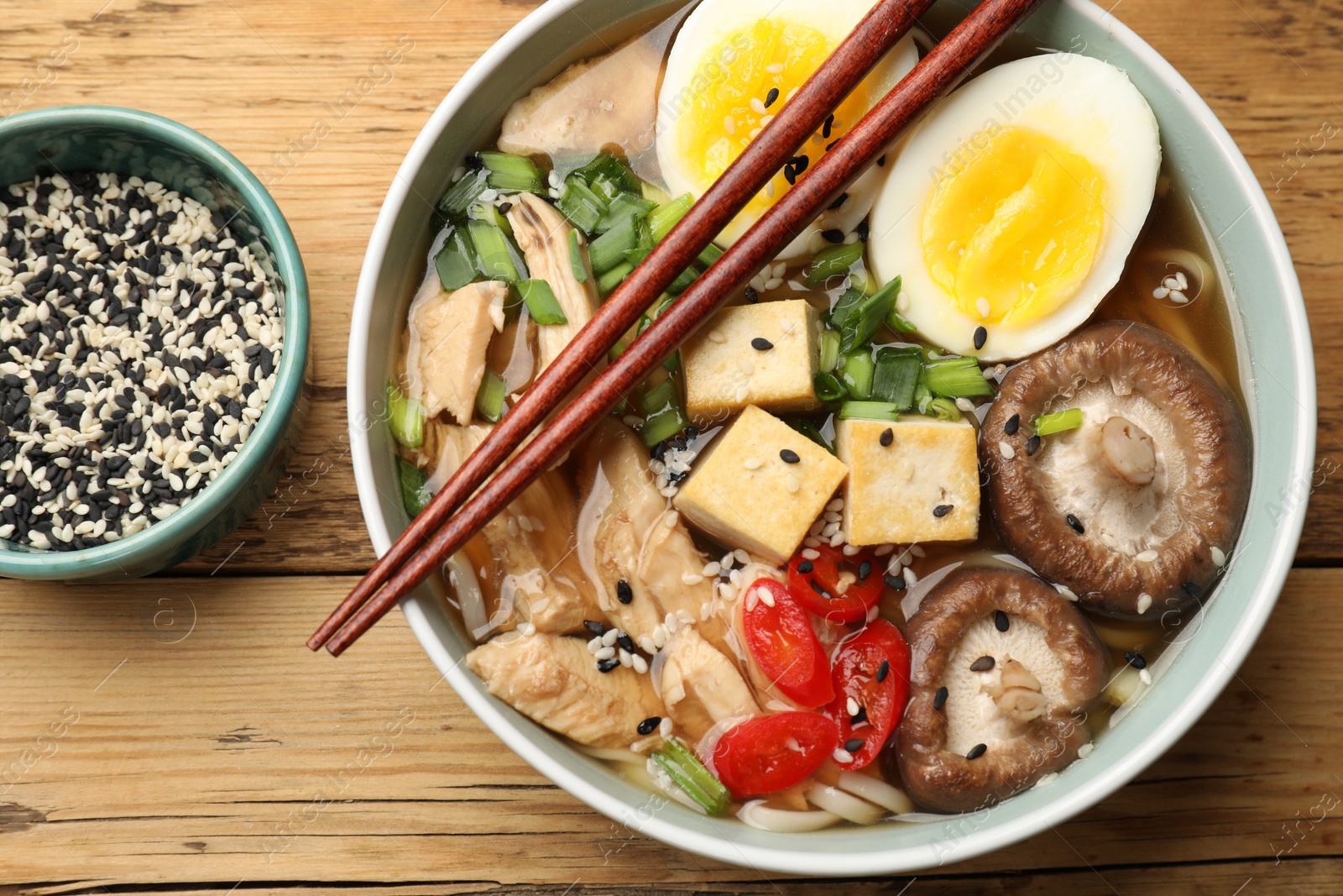 Photo of Bowl of delicious ramen and chopsticks on wooden table, flat lay. Noodle soup