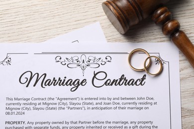 Marriage contract, golden wedding rings and gavel on wooden table, top view