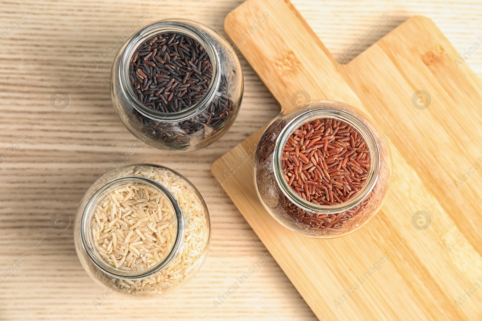 Photo of Jars with different types of rice and board on wooden table, top view