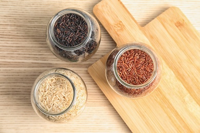 Jars with different types of rice and board on wooden table, top view