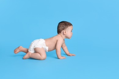 Photo of Cute baby in dry soft diaper crawling on light blue background