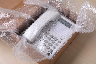 Corded phone with bubble wrap in cardboard box on wooden table, closeup