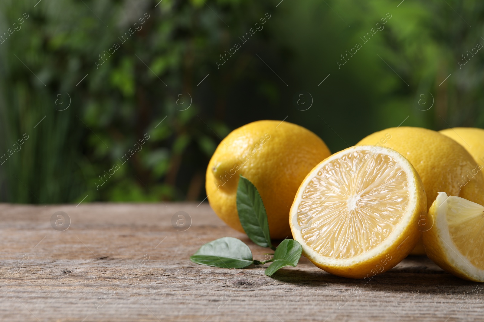 Photo of Fresh lemons and green leaves on wooden table outdoors, closeup. Space for text