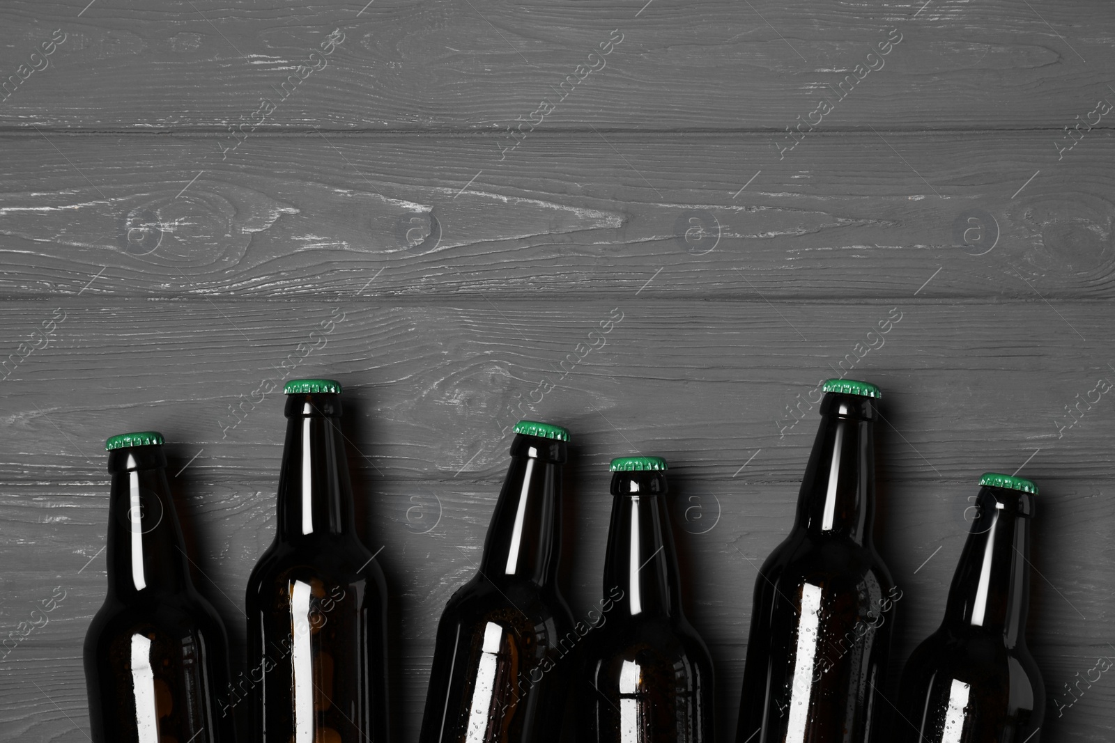 Photo of Glass bottles of beer on grey wooden background, flat lay. Space for text