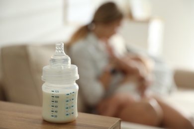 Photo of Mother breastfeeding her little baby at home, focus on bottle with milk. Healthy growth