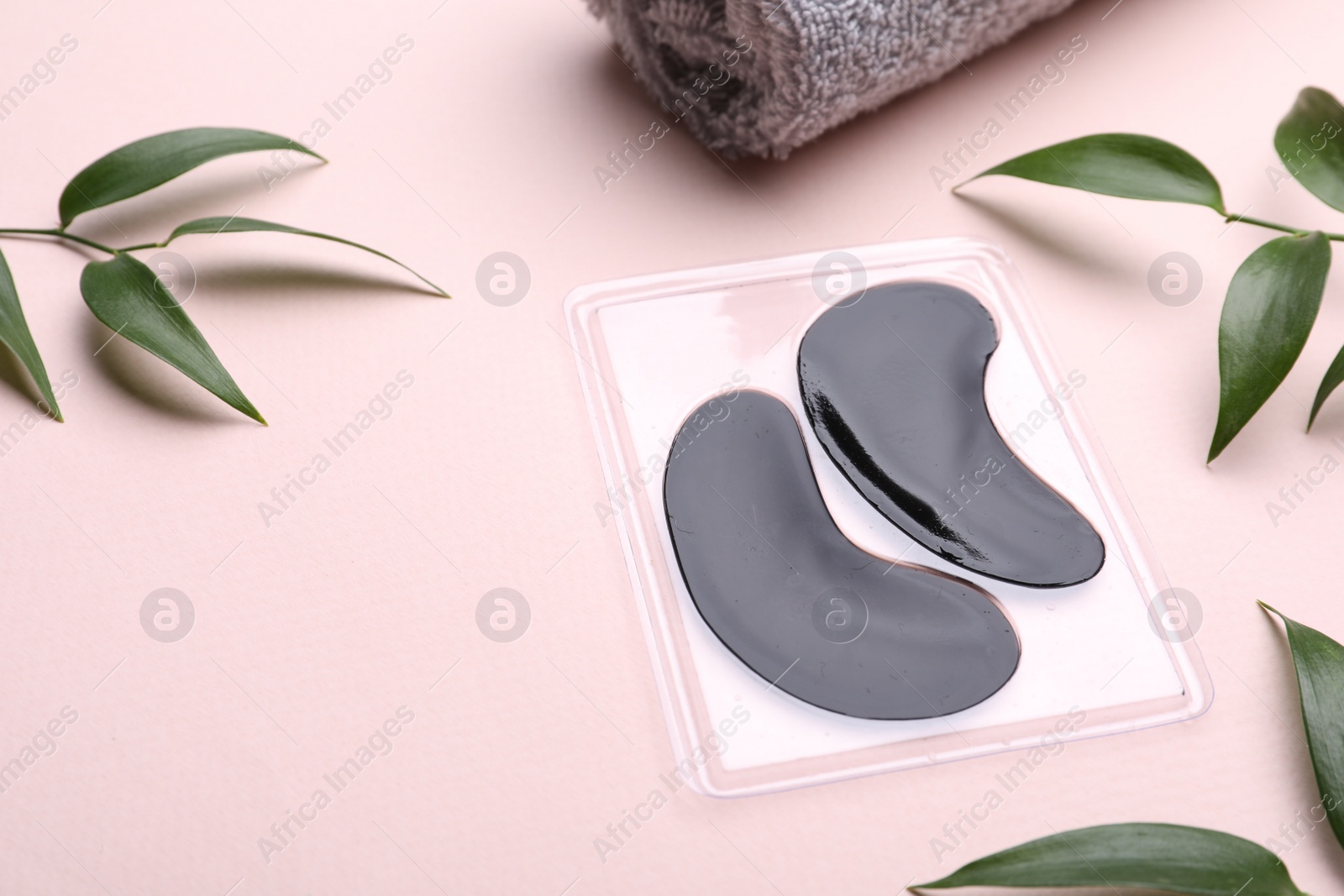 Photo of Package with under eye patches and green twigs on light pink background. Cosmetic product