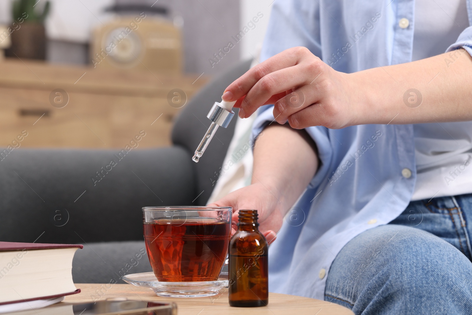 Photo of Woman dripping food supplement into cup of tea at wooden table indoors, closeup