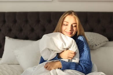 Photo of Beautiful young woman hugging soft blanket in bed at home. Winter atmosphere