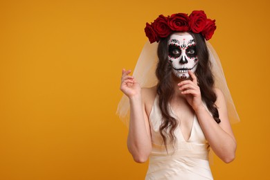 Photo of Young woman in scary bride costume with sugar skull makeup and flower crown on orange background, space for text. Halloween celebration