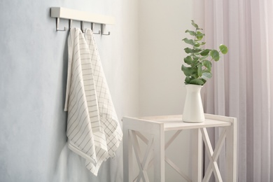 Photo of Hanger with kitchen towels and beautiful plant on table indoors. Interior design