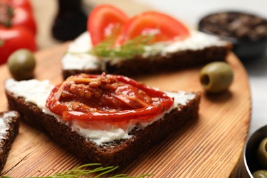 Delicious bruschetta with ricotta cheese and sun dried tomato on wooden board, closeup