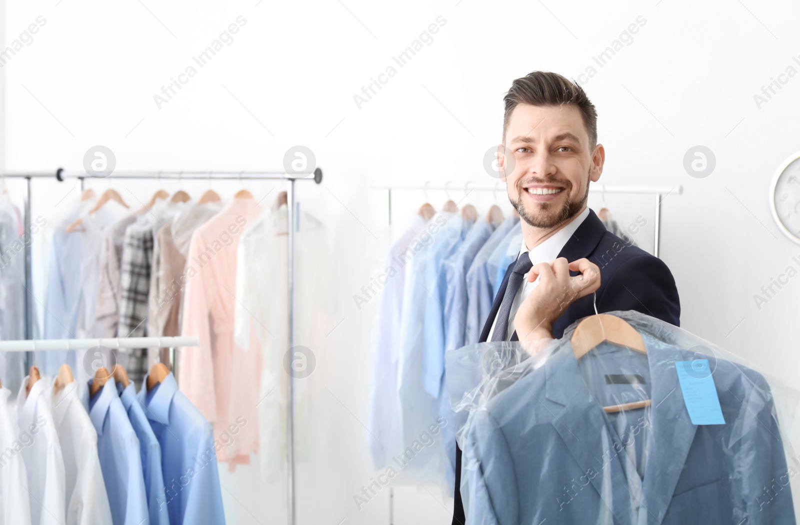 Photo of Young businessman holding hanger with jacket in plastic bag at dry-cleaner's