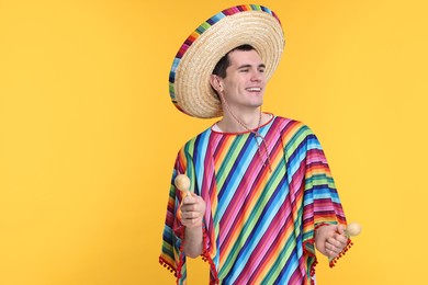 Photo of Young man in Mexican sombrero hat and poncho with maracas on yellow background. Space for text