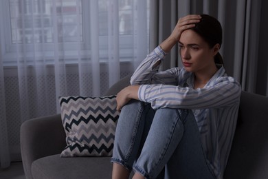 Photo of Unhappy young woman on sofa at home, space for text. Loneliness concept