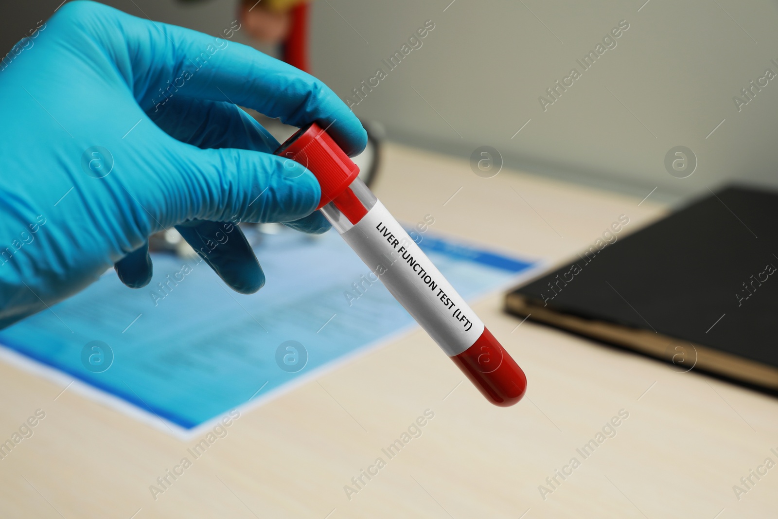 Photo of Laboratory worker holding tube with blood sample and label Liver Function Test over table, closeup