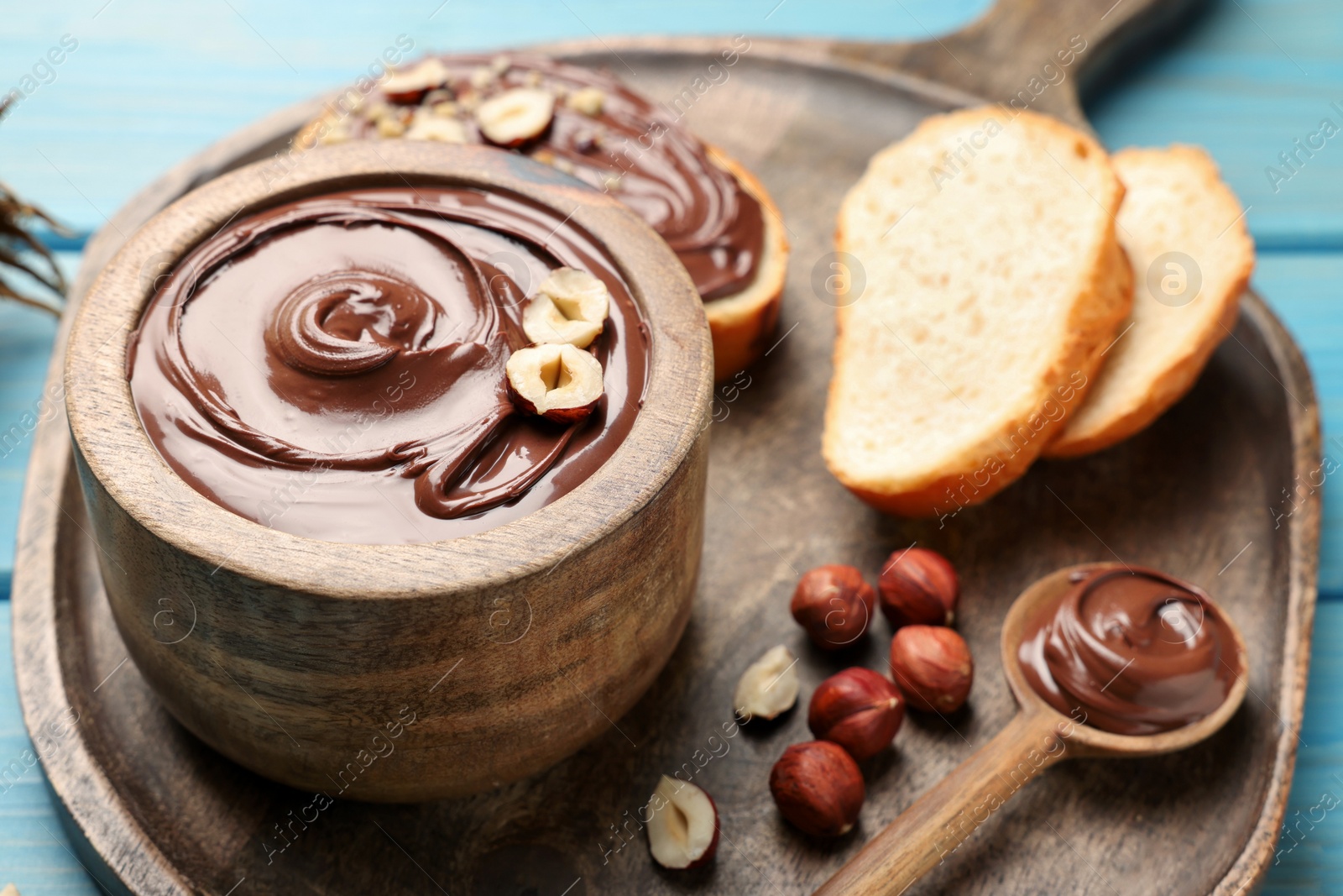 Photo of Bowl of tasty chocolate paste with hazelnuts on light blue wooden table, space for text