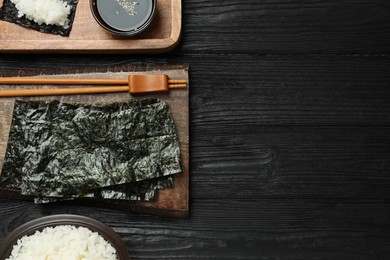 Photo of Dry nori sheets, rice, soy sauce and chopsticks on black wooden table, flat lay. Space for text