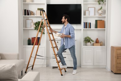 Man with books near wooden folding ladder at home