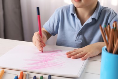 Photo of Little boy drawing with pencil at white wooden table indoors, closeup. Child`s art