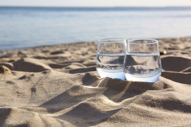 Sandy beach with glasses of refreshing drink on hot summer day, space for text