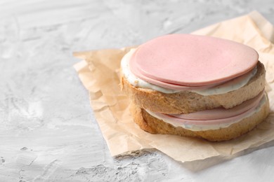 Photo of Delicious sandwich with boiled sausage and sauce on grey textured table, closeup. Space for text