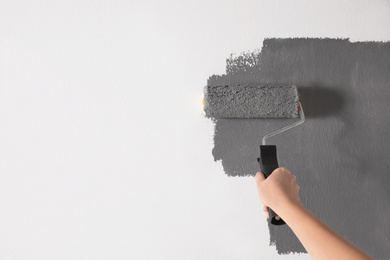 Photo of Woman painting white wall with grey dye, closeup. Space for text