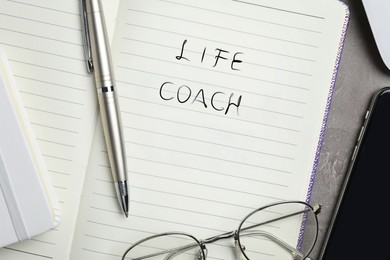 Phrase Life Coach written in notebook, pen and glasses on table, top view