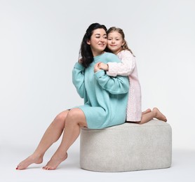 Beautiful mother hugging with little daughter on pouf against white background