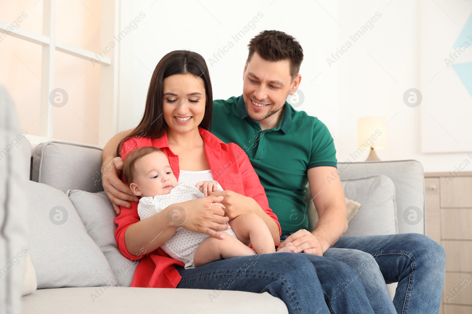 Photo of Happy couple with adorable baby on sofa at home. Family time