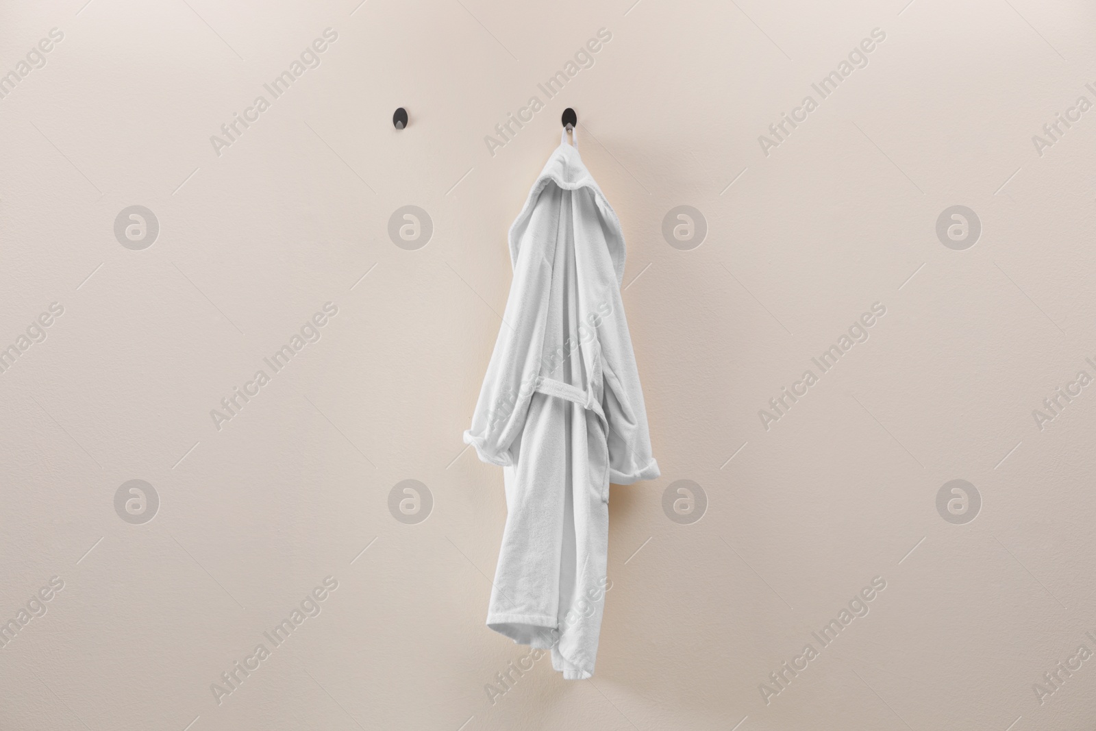 Photo of Soft comfortable bathrobe hanging on beige wall