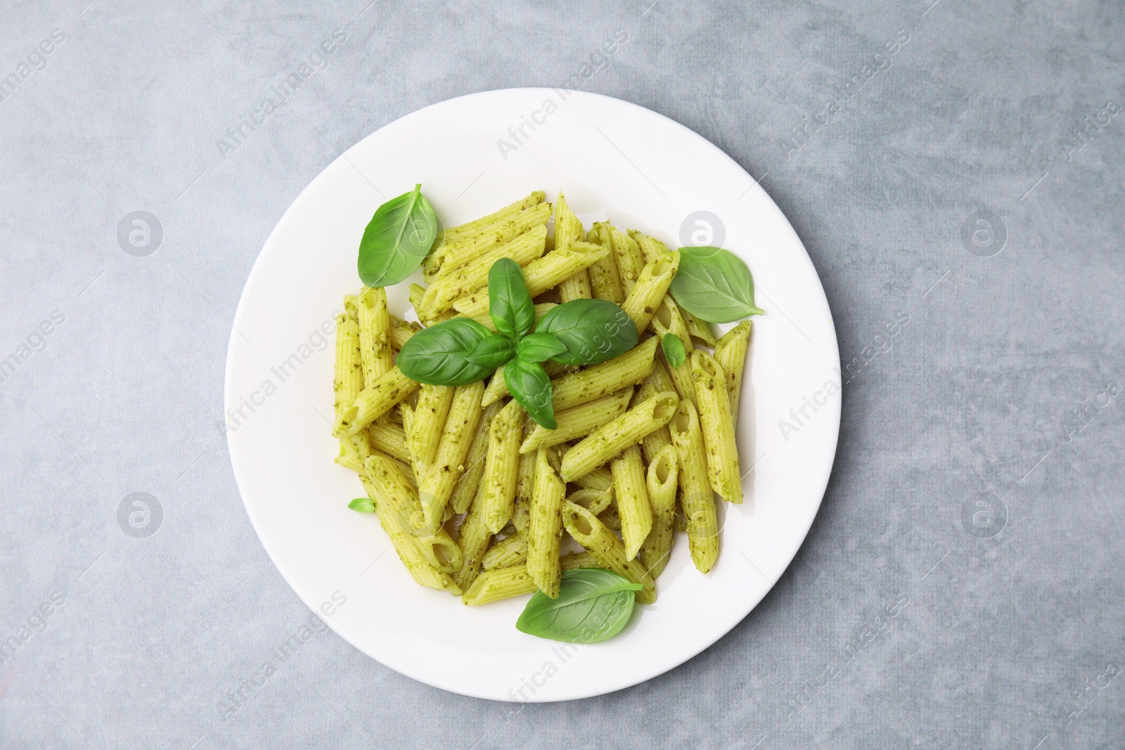 Photo of Delicious pasta with pesto sauce and basil on light grey table, top view
