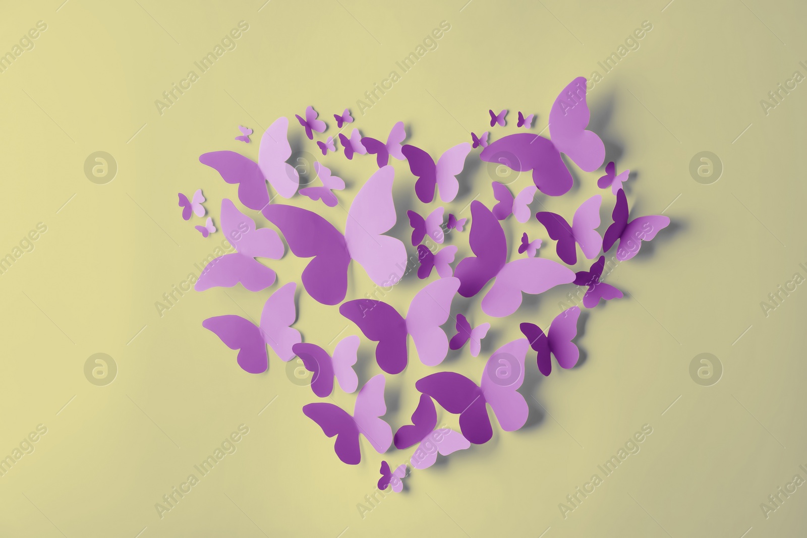 Image of Heart made of violet paper butterflies on light yellow wall