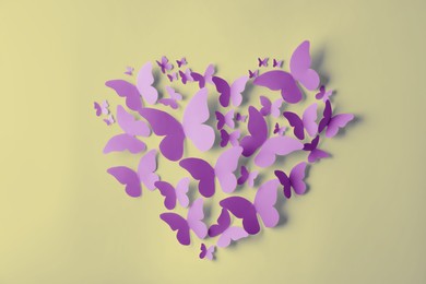 Heart made of violet paper butterflies on light yellow wall