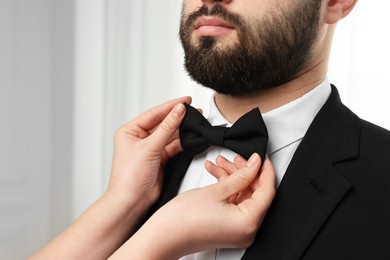 Photo of Woman adjusting bow tie to man indoors, closeup