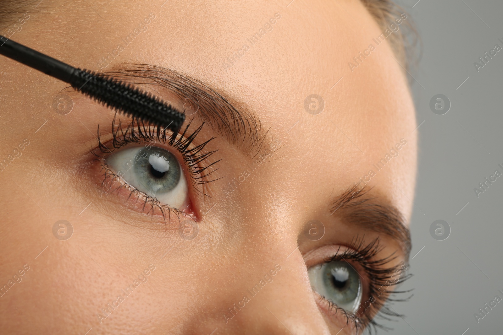 Photo of Woman applying mascara on grey background, closeup