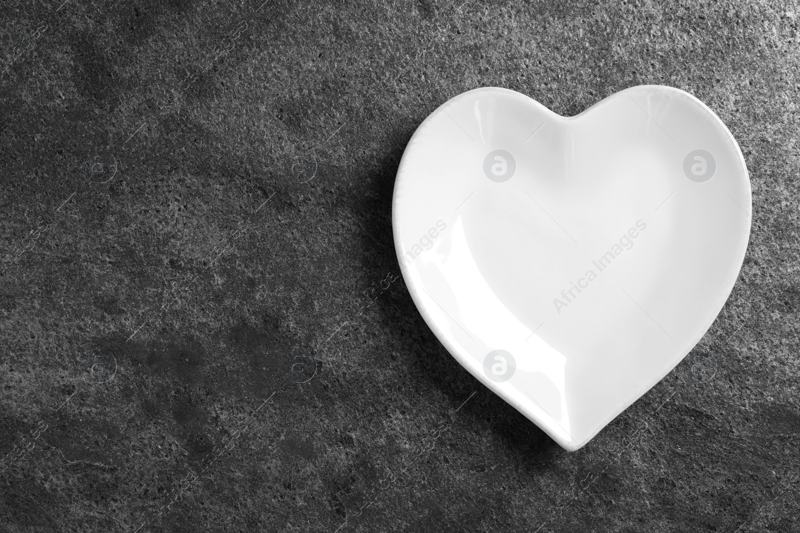 Photo of Heart shaped ceramic plate on grey table, top view. Space for text