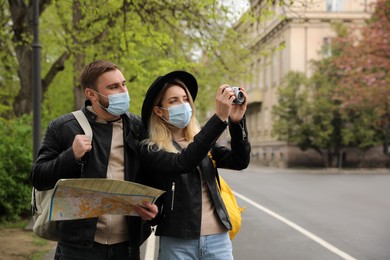 Photo of Couple of tourists in medical masks with map and camera on city street