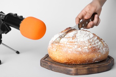 Woman making ASMR sounds with microphone and bread on grey background, closeup
