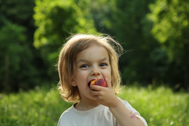 Photo of Cute little girl eating tasty peach in park