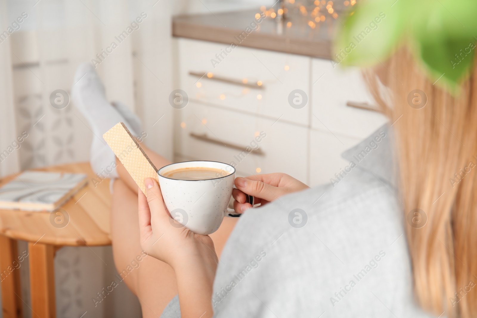 Photo of Woman having delicious wafer and coffee for breakfast indoors, closeup