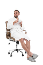 Photo of Handsome man with cup of coffee wearing bathrobe sitting in chair on white background