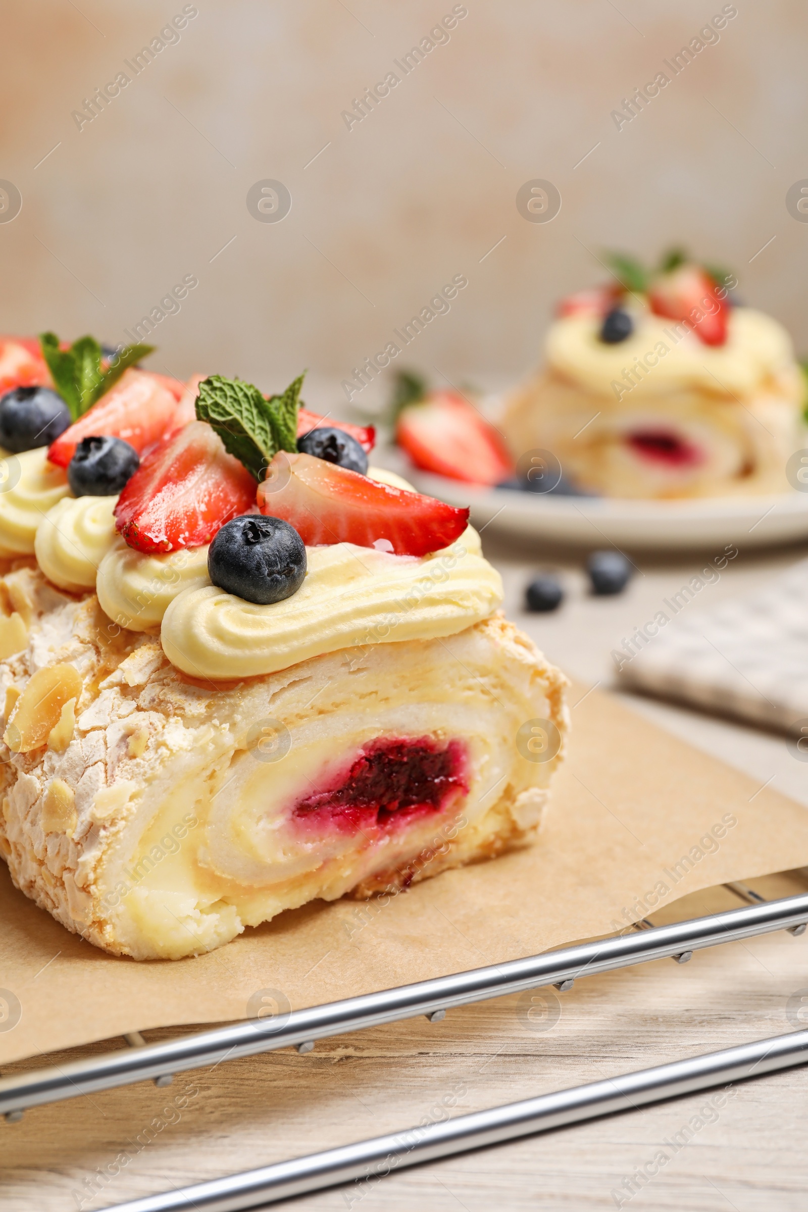 Photo of Tasty meringue roll with jam, cream, strawberry, blueberry and mint on white wooden table, closeup