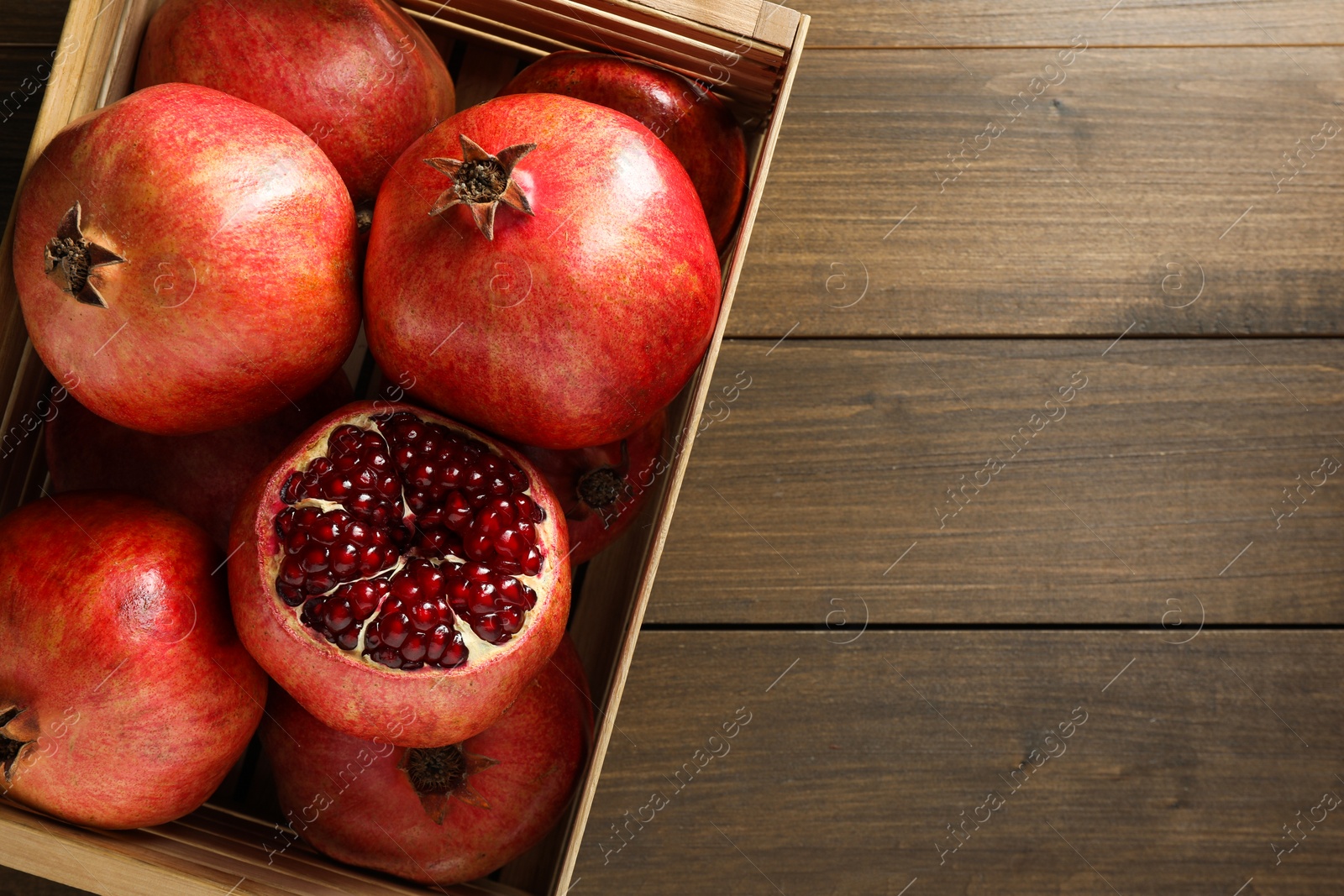 Photo of Ripe pomegranates in crate on wooden table, top view. Space for text