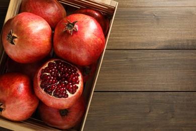 Ripe pomegranates in crate on wooden table, top view. Space for text