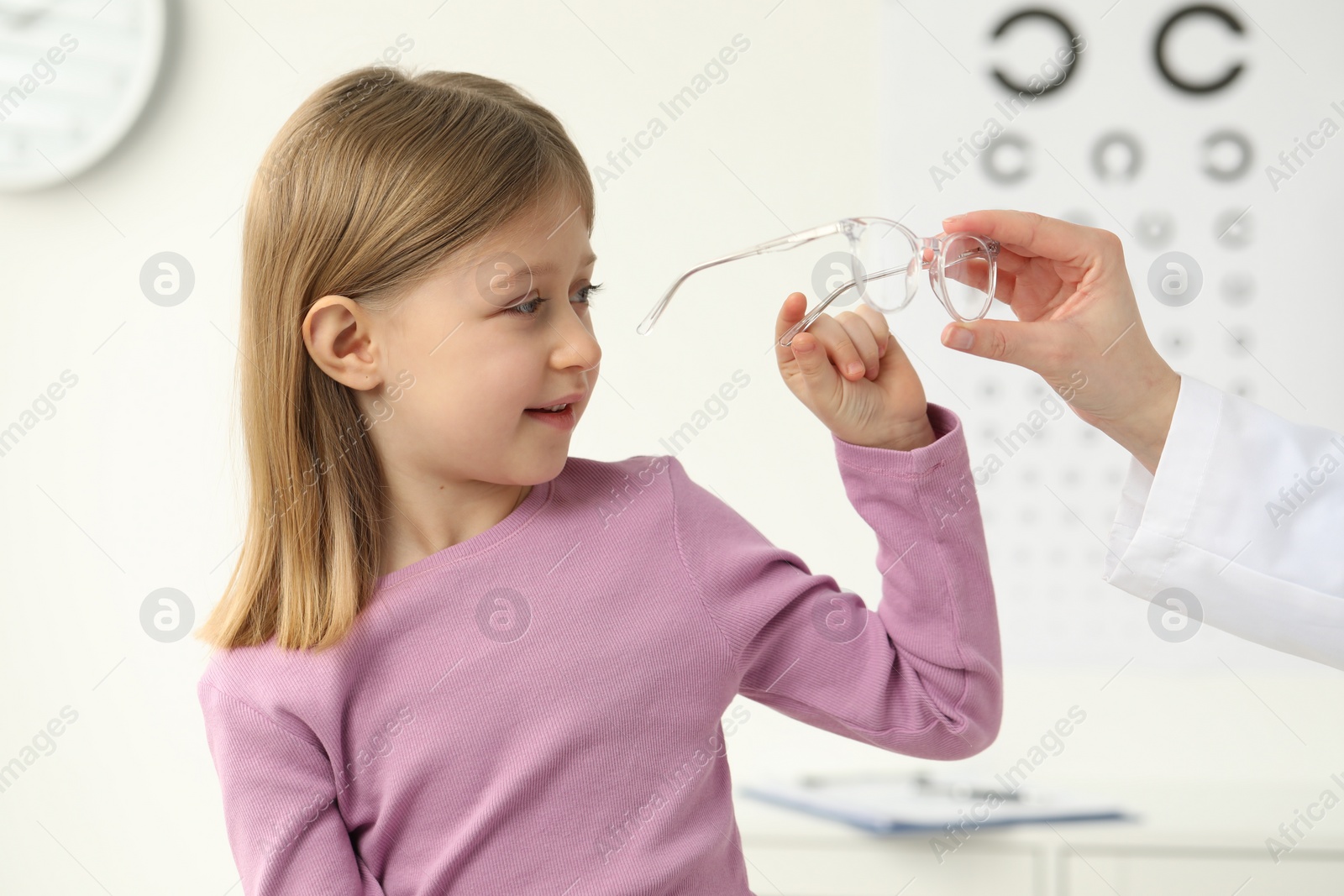 Photo of Vision testing. Ophthalmologist giving glasses to little girl indoors