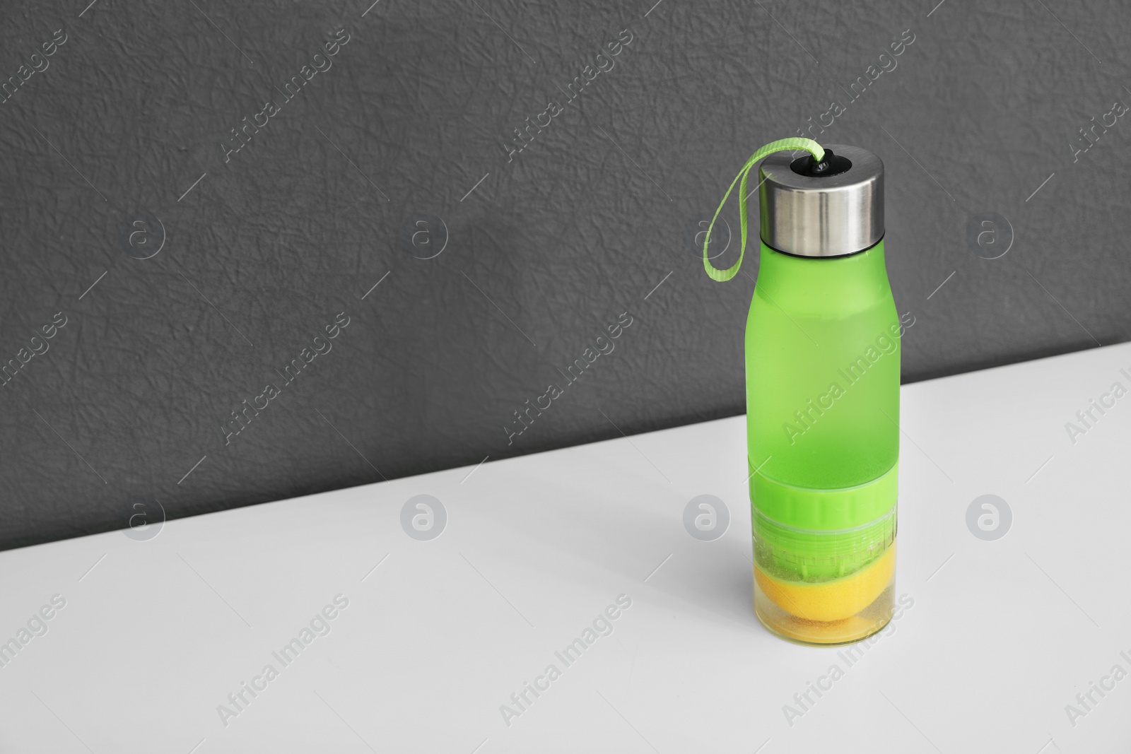 Photo of Sport bottle with lemon water on gray background. Space for text