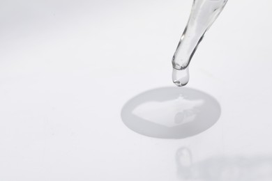 Glass pipette and transparent liquid on white background, closeup. Space for text