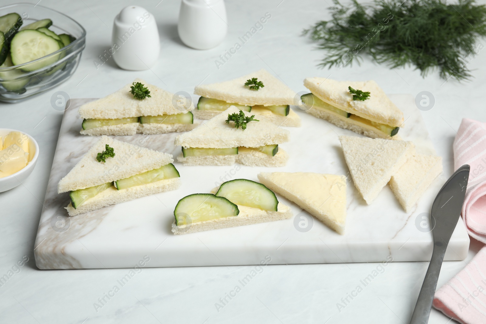 Photo of Tasty sandwiches with cucumber, butter and parsley on white marble table