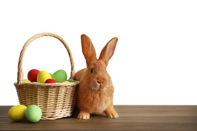 Photo of Cute bunny and basket with Easter eggs on wooden table against white background. Space for text